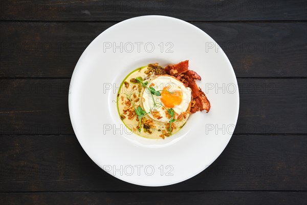 Top view of fried egg with bacon slices and chips served with creamy sauce