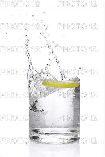 Ice cube and lemon splashing cocktail in oldfashioned glass. Drink with splashing citrus isolated on white