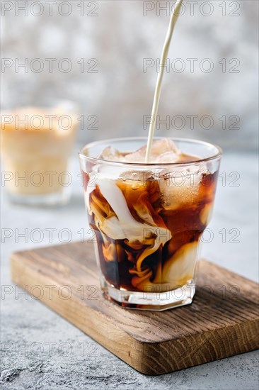 Pouring cream in iced coffee in rocks glass