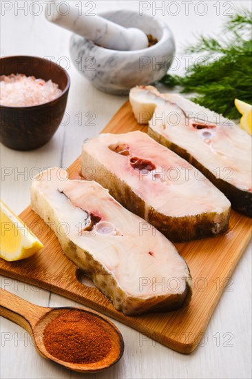 Top view of fresh raw cod steak on wooden cutting board with spice