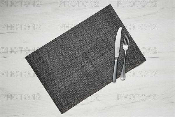 Top view of gray placemat table mat with knife and fork on white wooden table