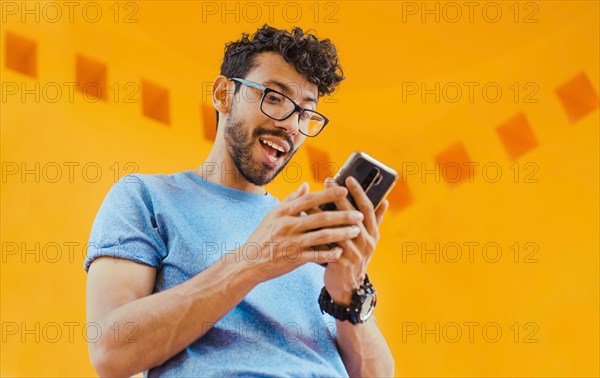 Happy guy sending a message with a cell phone near a yellow wall outdoors. Lifestyle of handsome bearded man using cell phone outdoors