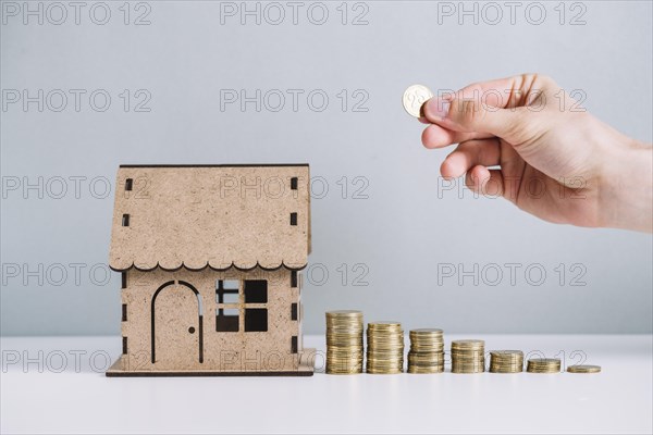 Person s hand stacking coins near house model