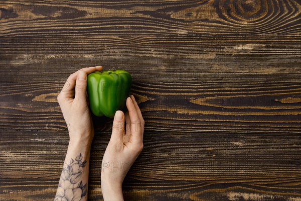 Overhead view of fresh green bell pepper in hands over wooden background