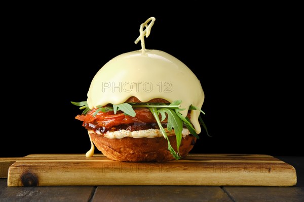 Burger with beef and top bun covered with melting cheese on wooden serving board over black background