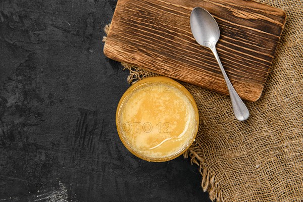 Top view of pot with honey and spoon on wooden serving board