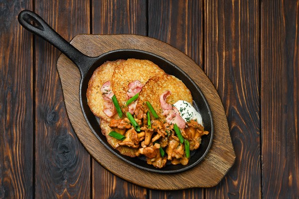 Top view of potato pancakes with chanterelles and pork in cast iron skillet