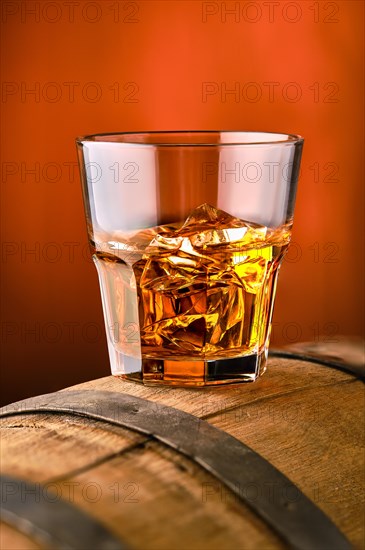 Glass of whisky with ice on the top of barrel