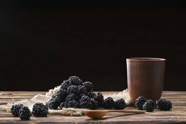 Heap of fresh dewberry on sackcloth table-napkin and clay cup with milk on wooden table