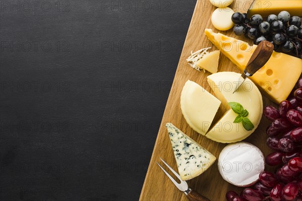 Flat lay mix of gourmet cheese and grapes on cutting board with copy space