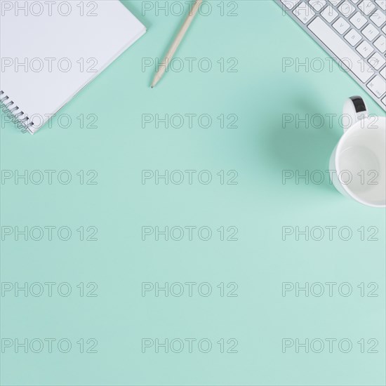 Close up blank notepad pencil cup keyboard turquoise background with space text