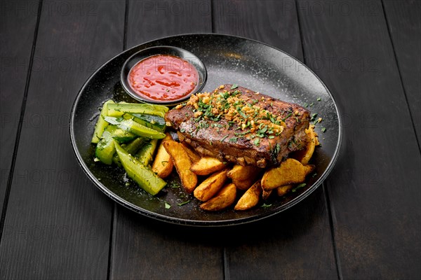 Roasted beef ribs with potato wedges and pickled cucumber on a plate