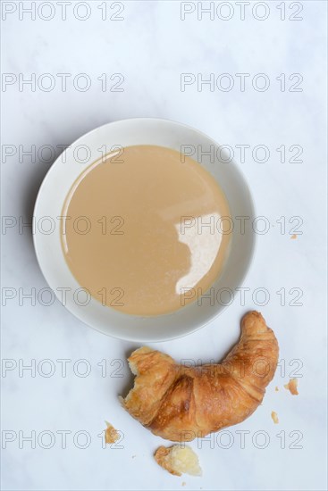 Coffee with milk in bowl and croissant