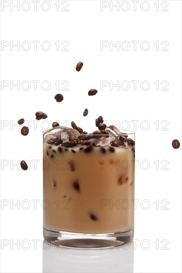 Coffee beans falling into cocktail with Irish creme liqueur in a glass full of ice
