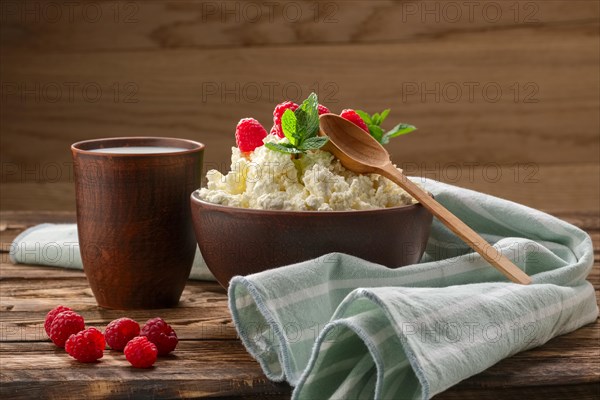 Cottage cheese with wooden spoon on it and milk in clayware on wooden table