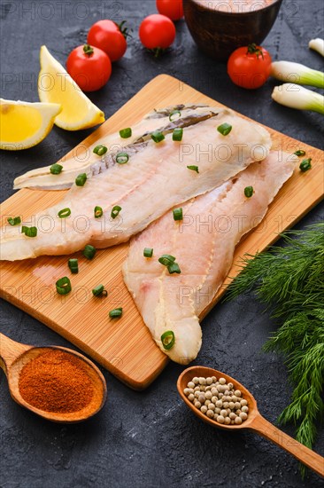 Raw fresh haddock fillet on wooden cutting board with spice and herbs