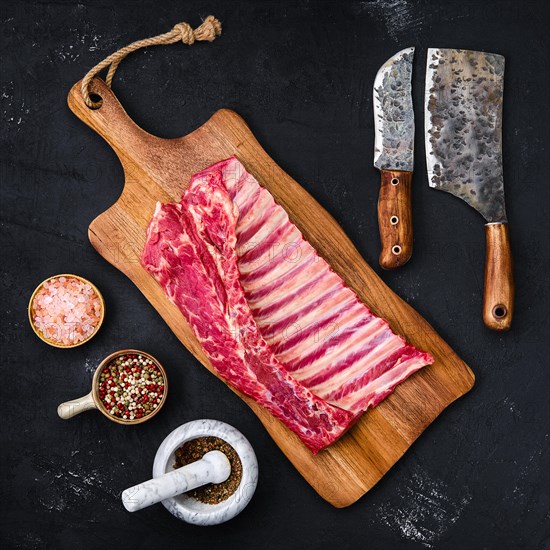 Fresh raw rack of lamb on wooden cutting board with herbs and seasoning