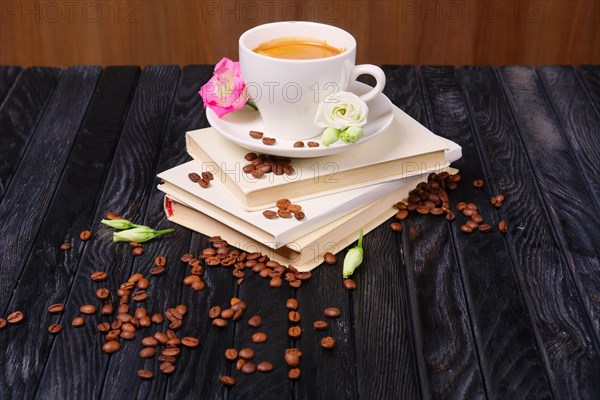 Cup of coffee on top of books pile with coffee beans and flowers scattered on the table