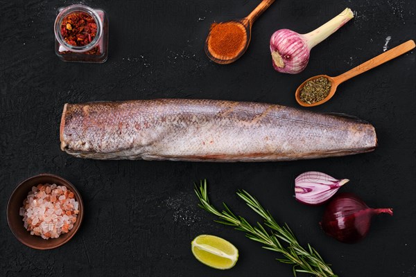 Raw hake with spice on black background