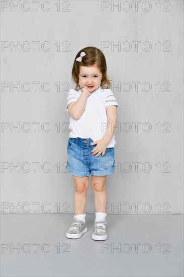 Two years old girl in white t-short and jeans shorts posing in studio