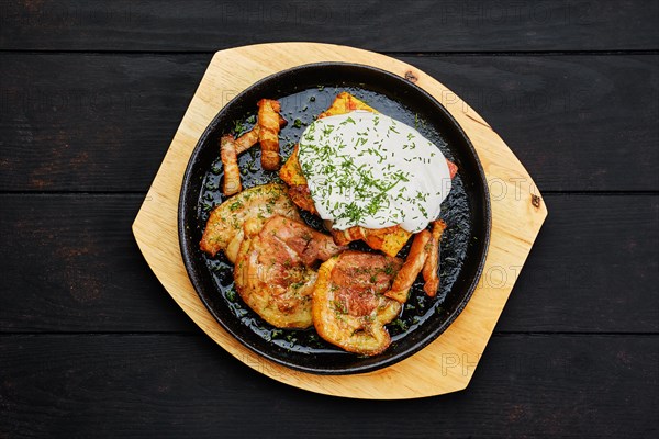 Top view of potato casserole with fried pork mini belly slices on dark wooden table