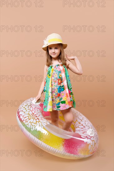 Cute child in sundress and straw hat with swimming ring playing in studio