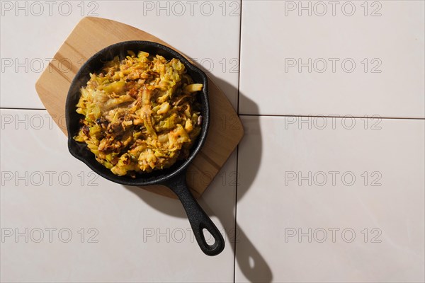 Top view of stewed cabbage and zucchini in cast iron skillet on ceramic tile background with harsh shadow