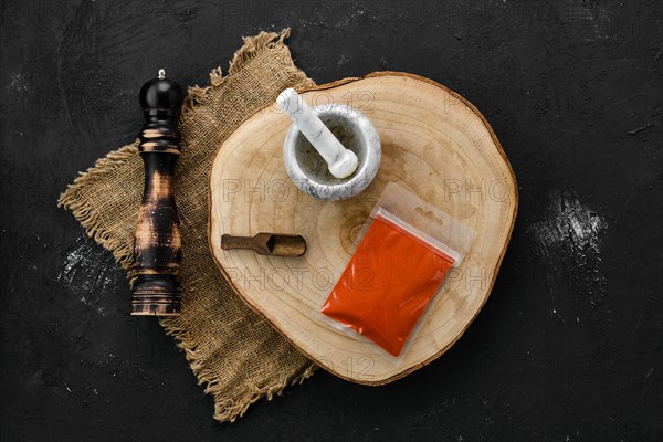 Wooden cross section with smoked paprika in plastic package and stone mortar and mill