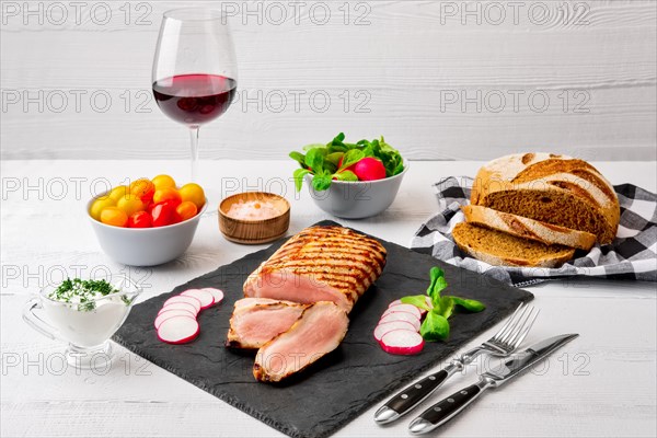 Sliced grilled pork fillet with fresh tomatoes and raddish served with glass of red wine