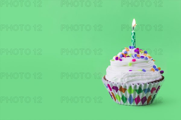 Close up delicious cupcake with burning candle green background