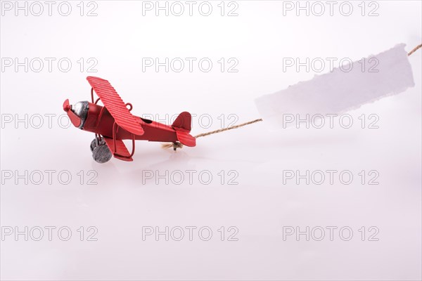 Red plane flying with a paper after it on a white background