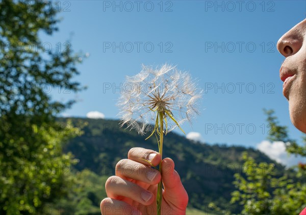 Boy blowing a Dandelion seed in hand against green nature background