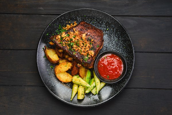 Top view of juicy grilled pork ribs with potato wedges and cucumber
