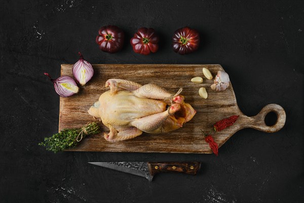 Raw whole chicken with spices on wooden cutting board