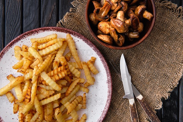 Fried crinkle cut american fries and roasted mushrooms on dark wooden table