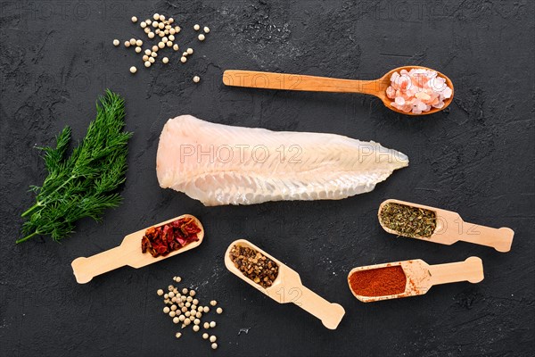 Raw shallow-water hake fillet with spice and herbs on black concrete background