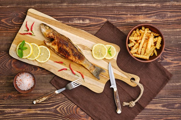 Top view of fried sea bass with fried potato on wooden cutting board