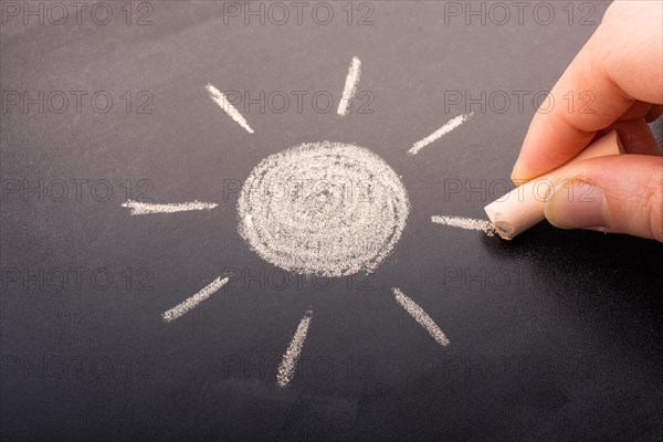 Hand drawing sun by chalk with light ray shape on blackboard background