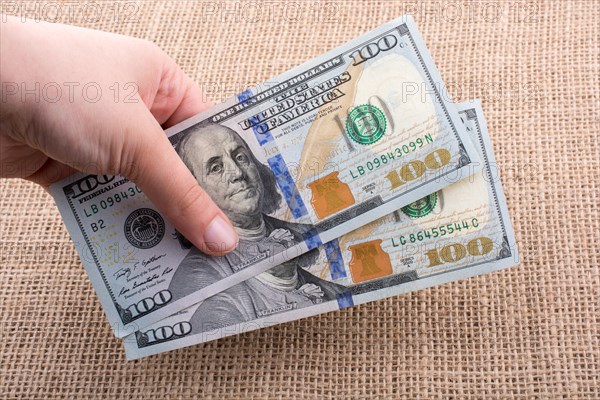 Hand holding banknote bundle of US dollar on a linen canvas background