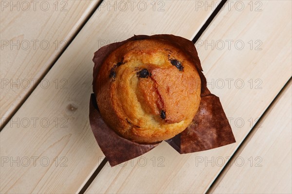 Top view of fresh muffin with chocolate chips in paper wrapper on wooden table