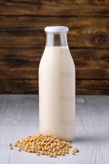 Bottle of soy milk with soybeans on white table over dark wooden background