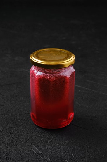 Whole closed jar of cherry jam on black background