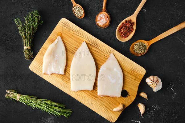 Overhead view of raw frozen squid fillet on wooden cutting board