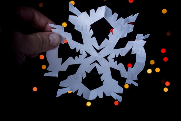 Snowflake shaped paper in hand on bokeh light background