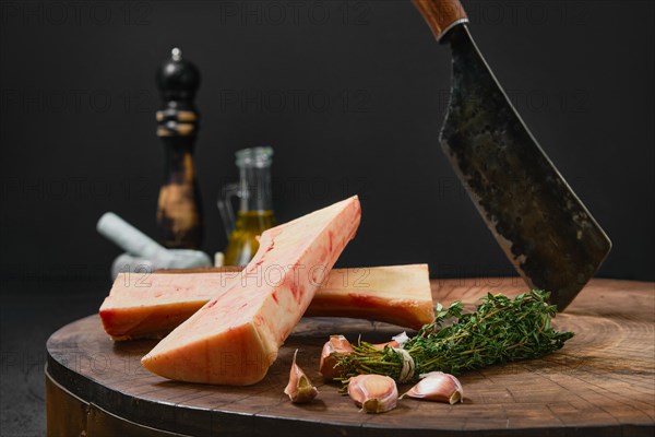 Large beef bone marrow chopped on half with spice and herbs on wooden stump