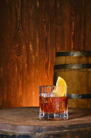 Cocktail with blended malt scotch whisky and orange bitter with a barrel on background