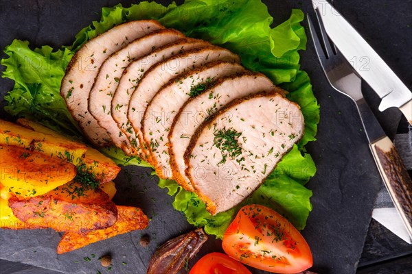 Sliced baked ham with fresh tomatoes on a stone plate in a rustic style