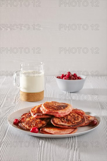 Pancakes with cherry and glass of milk on white kitchen table