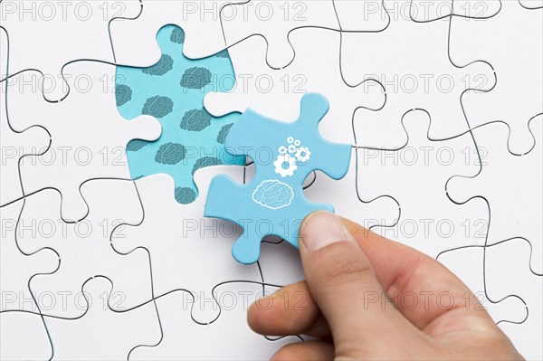 Close up human hand holding blue puzzle piece with brain cogwheel drawing