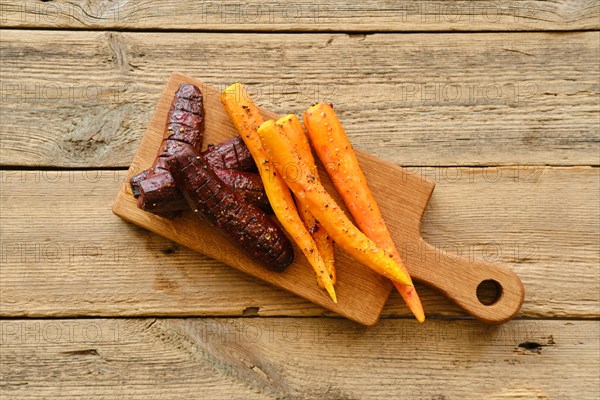 Overhead view of baked carrot and beetroot with salt and pepper on wooden board